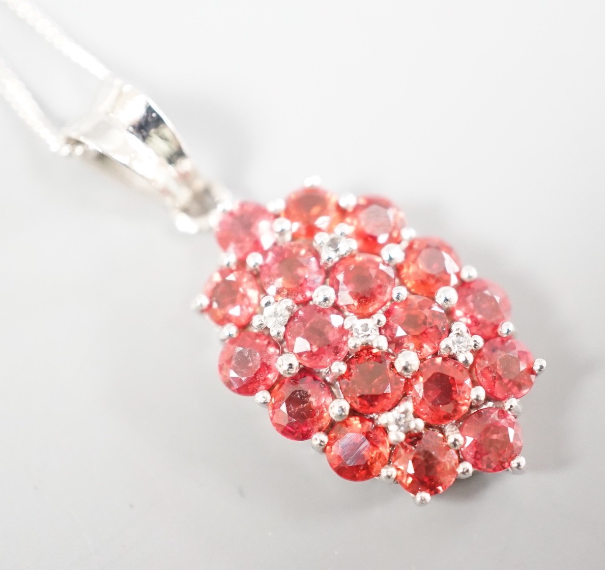 A modern 375 white metal, sunset ruby and white sapphire set cluster pendant, 19mm, on a 375 white metal chain, 42cm, gross 4 grams, with Rocks & Co certificate.